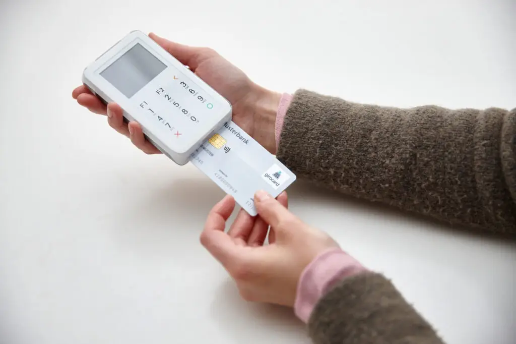Hände halten ein mobiles Kartenlesegerät und eine Kreditkarte, die in das Gerät eingeführt wird, um eine Zahlung zu tätigen.