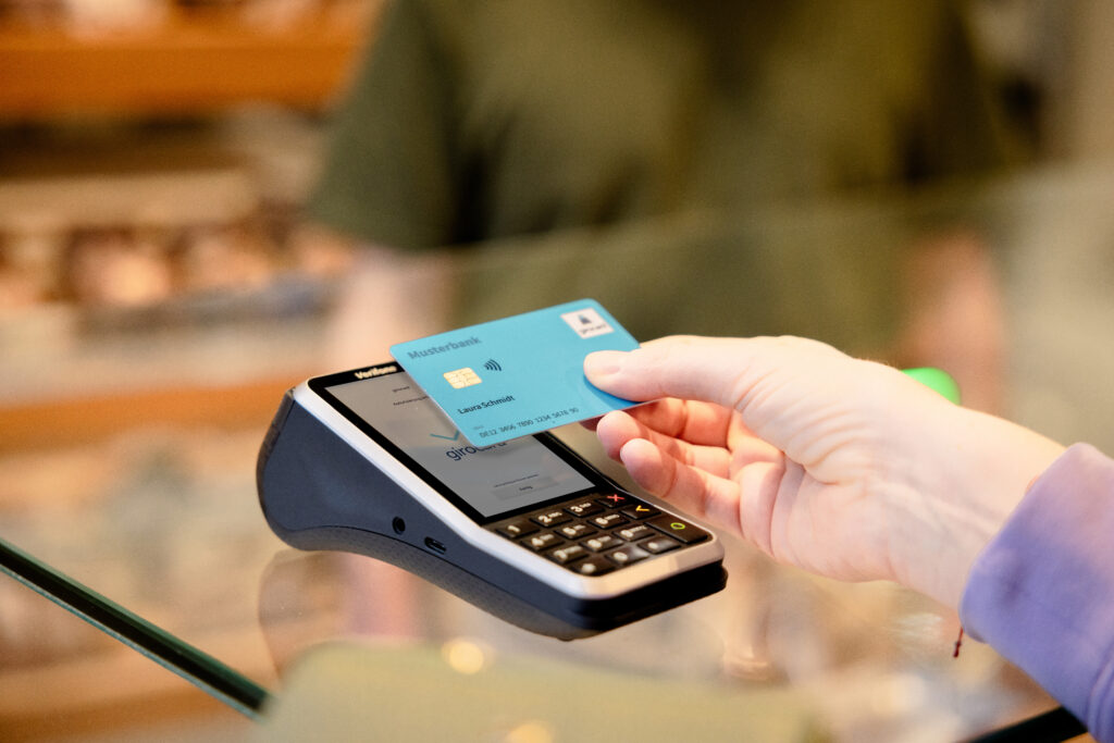 Eine Hand hält eine girocard an ein Terminal um kontaktlos zu bezahlen.