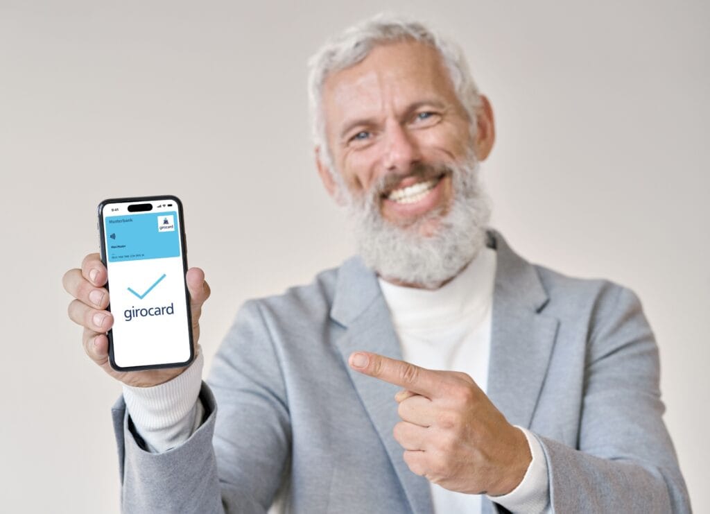 Ein freundlich lächelnder, älterer Mann zeigt auf sein Handydisplay, auf dem eine digitale Musterkarte zu sehen ist.