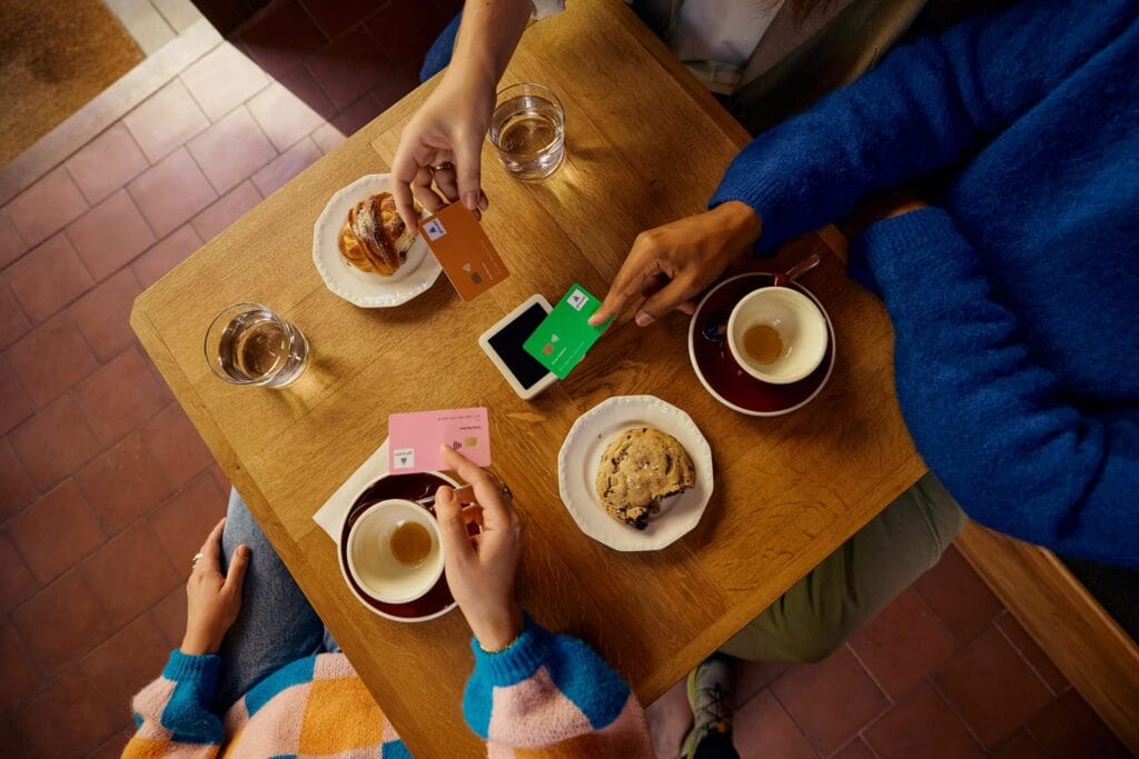 In einem Café halten drei Personen ihre girocard an ein Terminal, um kontaktlos zu bezahlen.