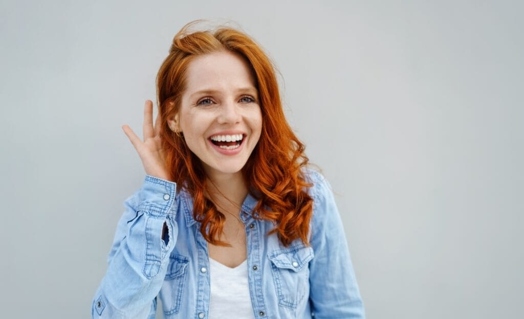 Eine junge, rothaarige Frau mit weißem Shirt und Jeansjacke lächelt freundlich.
