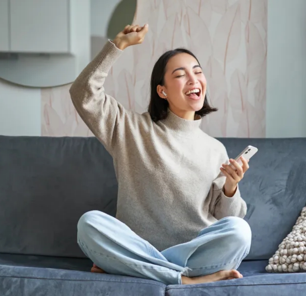 Eine Frau sitzt auf dem Sofa und hält ihr Smartphone in der Hand.