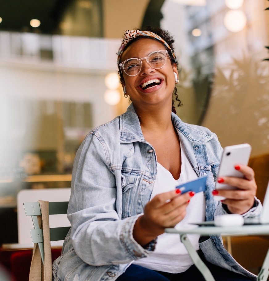 Eine Frau lacht in die Kamera und hält eine girocard und ein Smartphone in ihren Händen.